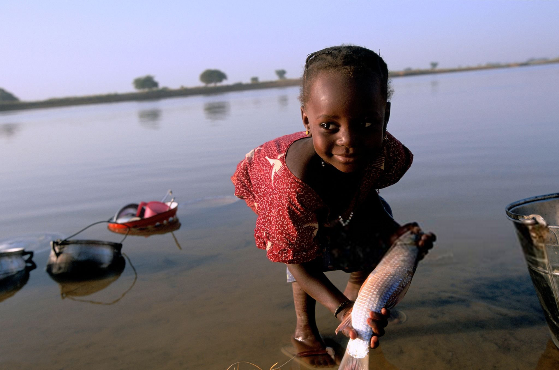A little girl of Diafarabe Fulani's village on the banks of the River Niger, cleans her clothes and a fish for lunch, Niger.