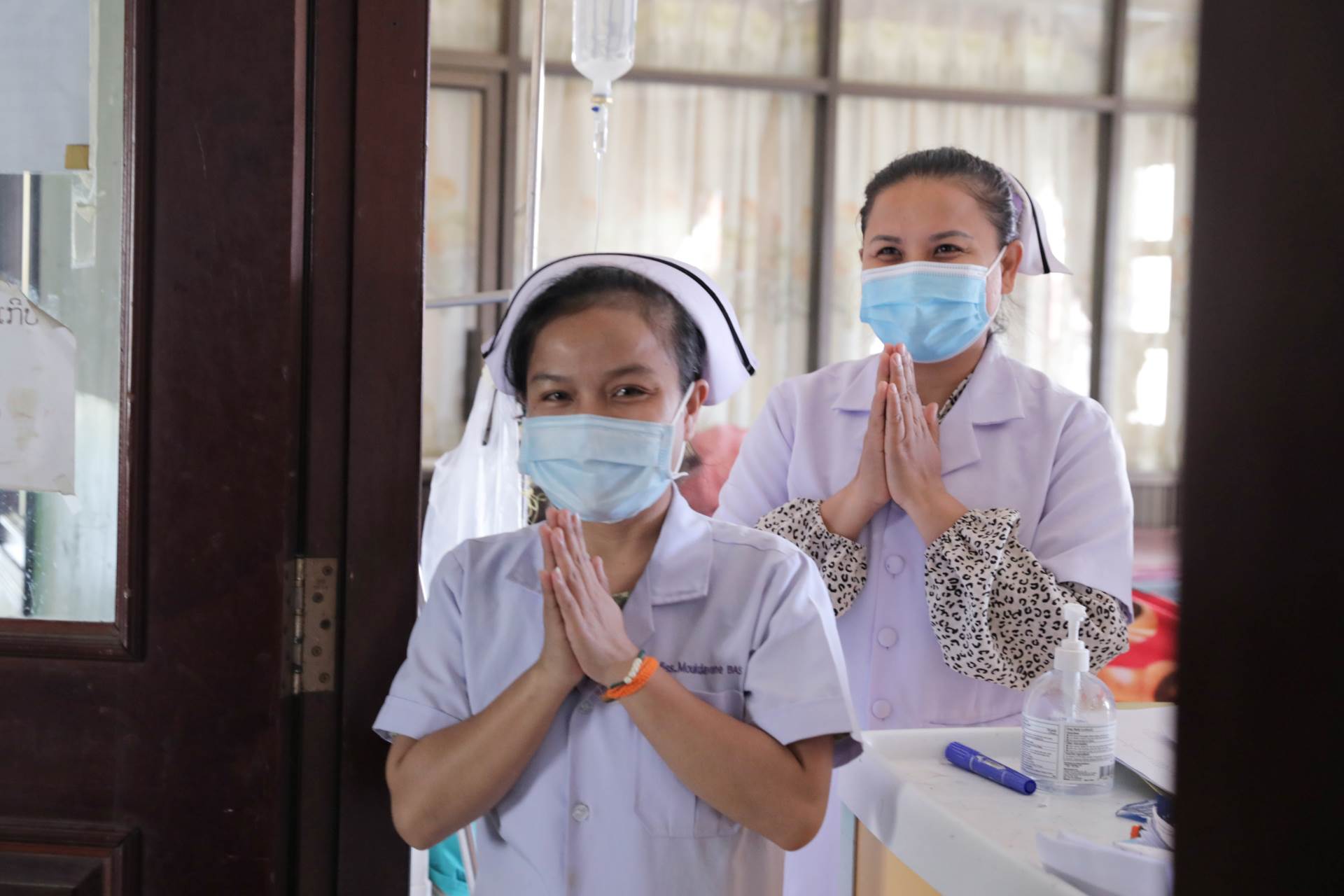 Two nurses with hands joined greet patients in a clinic